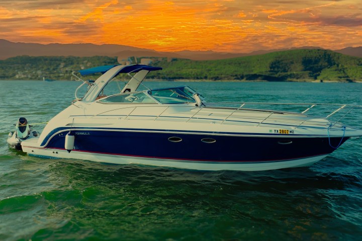 A white and blue speedboat on a lake with a sunset background.