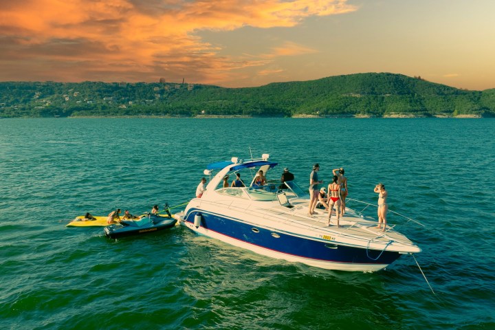 People on a yacht in a lake with sunset sky and green hills in the background.